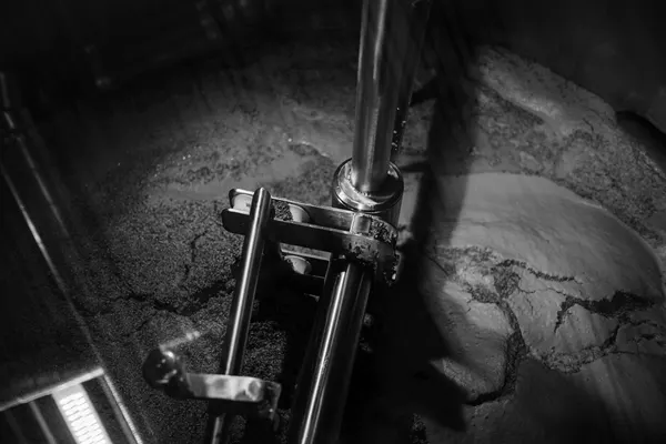 Braccio di un agitatore industriale che rimescola un impasto denso dentro un recipiente d’acciaio, ripreso dall’alto in bianco e nero