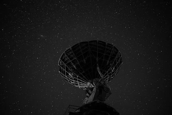Antenna paraboloide in bianco e nero, ripresa dal basso, stagliata contro un cielo notturno pieno di stelle