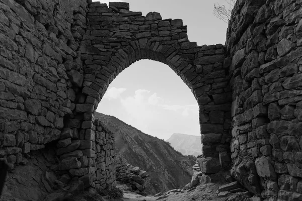 Un arco costruito a pietra a secco, senza malta, che regge un varco fra due muri di roccia, in bianco e nero