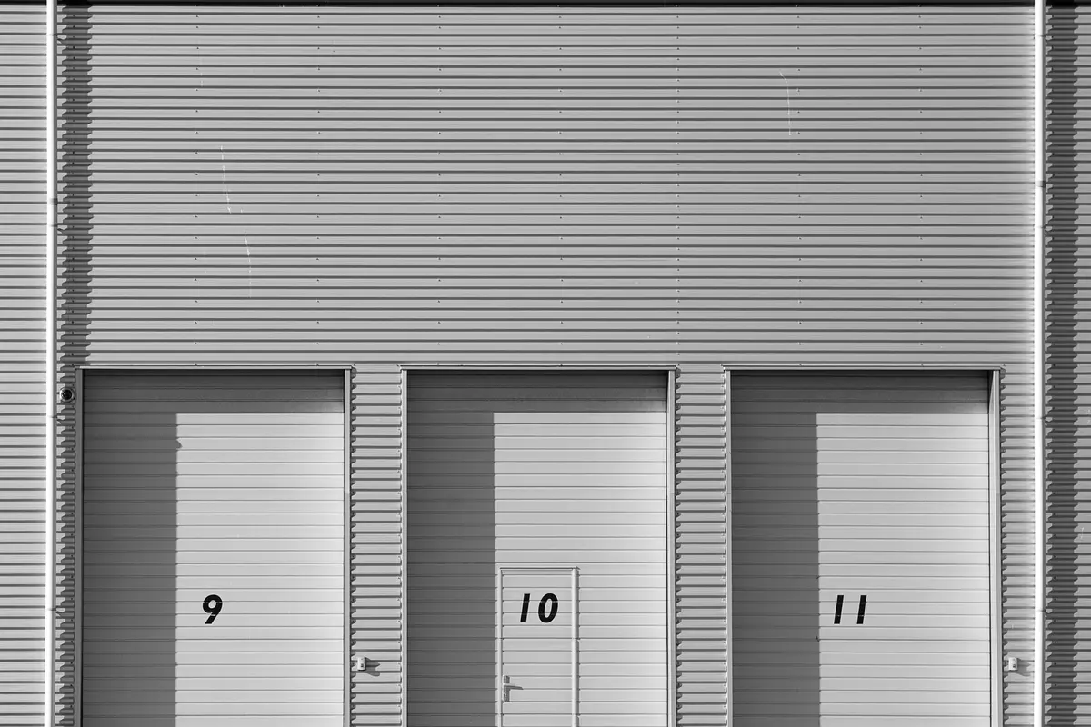 Industrial corrugated-metal facade with three numbered roller-shutter doors, 9, 10 and 11, black-and-white photograph