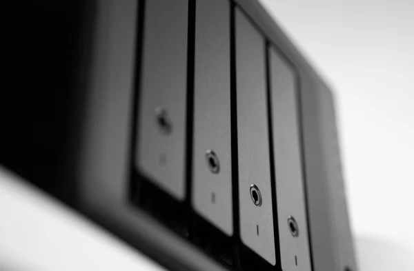 Vista ravvicinata e in prospettiva di un modulo di storage nero con vani identici, ciascuno con una piccola serratura e un indicatore verticale, sfondo bianco sfocato, fotografia in bianco e nero