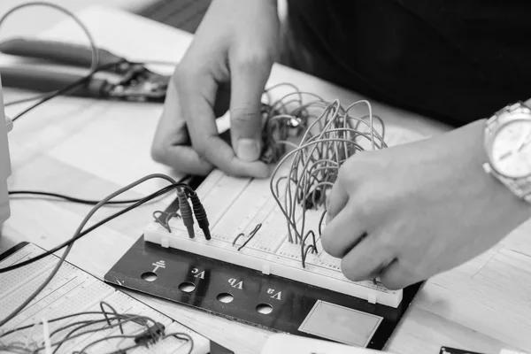 Two hands connecting wires on a breadboard linked to measurement probes, in black and white