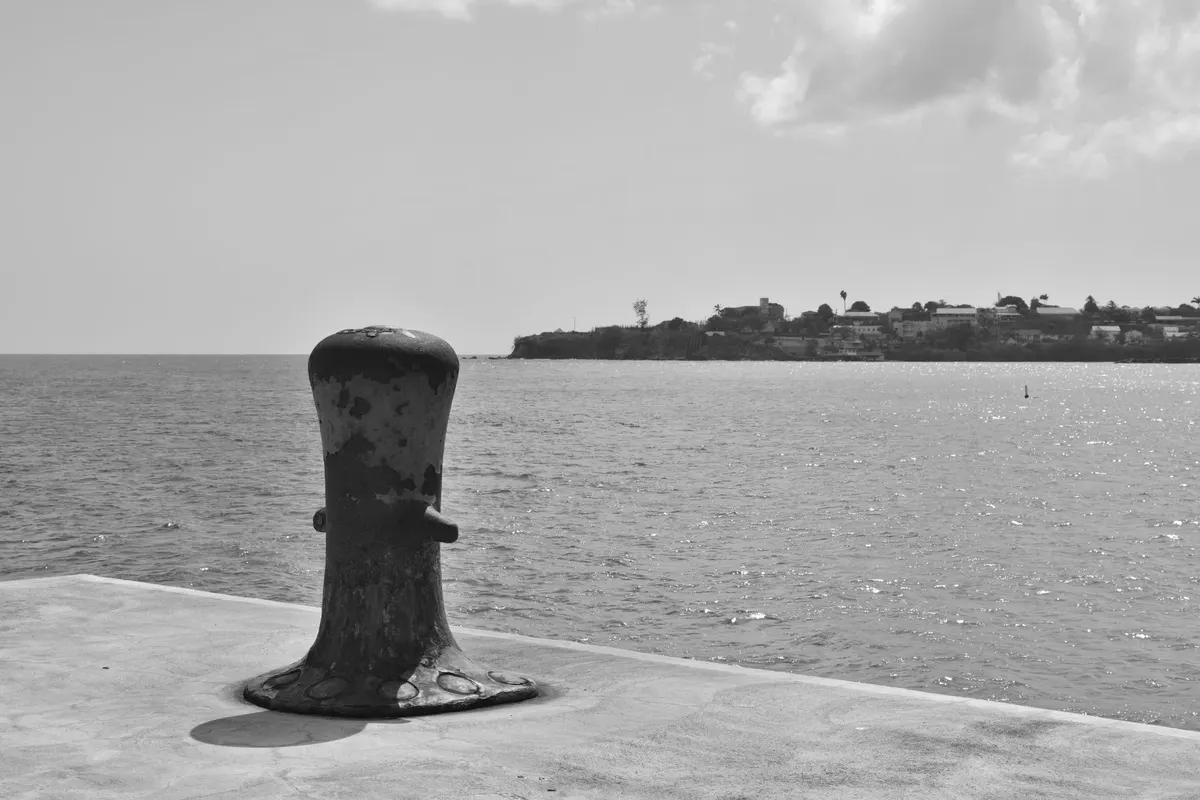 A rusted mooring bollard on a deserted concrete quay, open sea behind it, black and white photograph