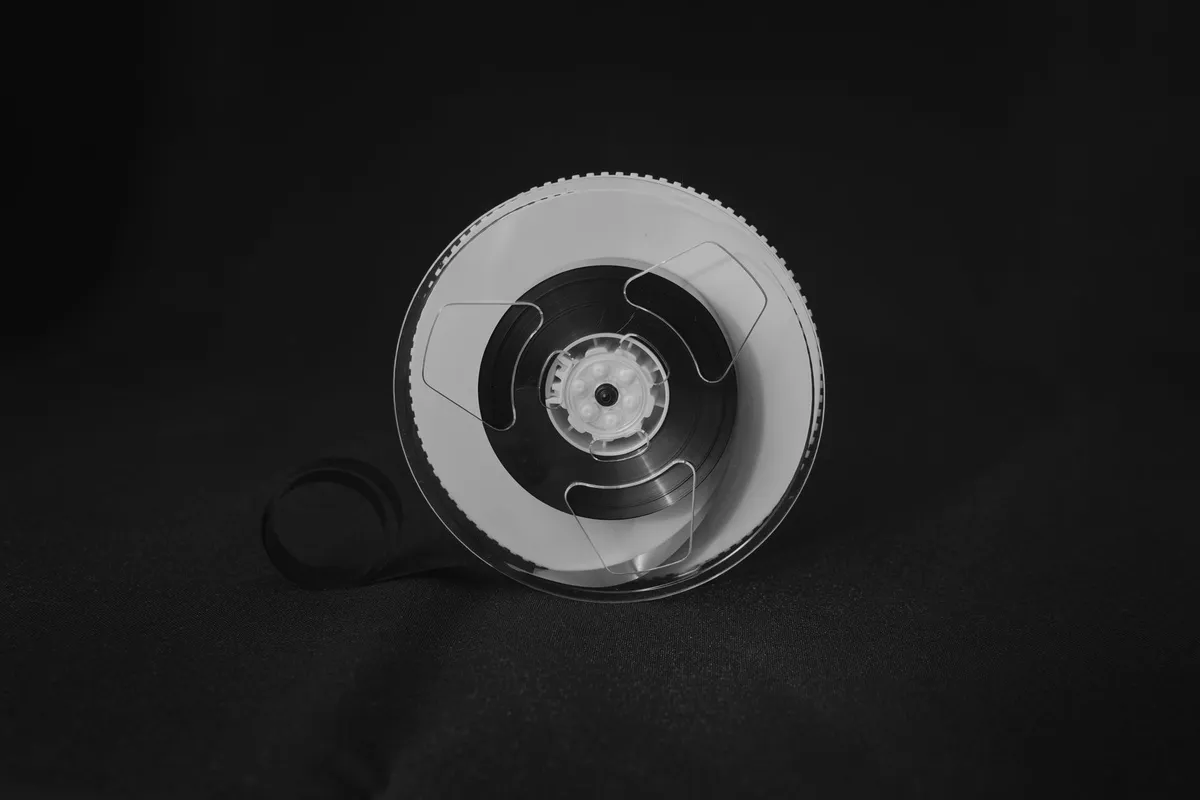 Bobina di nastro magnetico per registrazione dati, appoggiata su fondo scuro, con un lembo di nastro srotolato, in bianco e nero