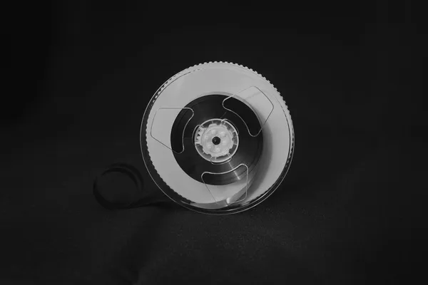 Bobina di nastro magnetico per registrazione dati, appoggiata su fondo scuro, con un lembo di nastro srotolato, in bianco e nero