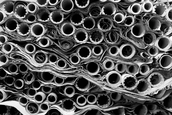 Parete fittissima di rotoli di carta visti di testa, decine e decine, impilati in file irregolari, fotografia in bianco e nero; nessun rotolo è identificabile, non ci sono persone, loghi né scritte leggibili