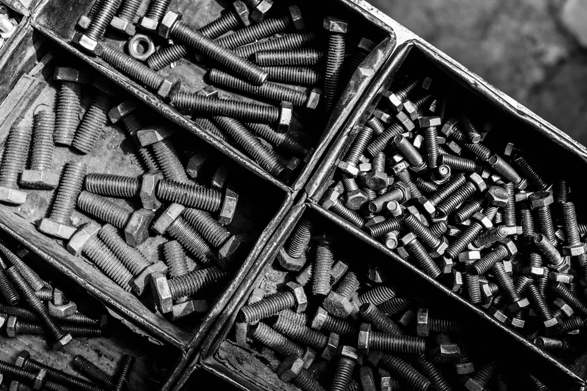 Metal compartments filled with bolts and nuts of different sizes, shot from above in black and white
