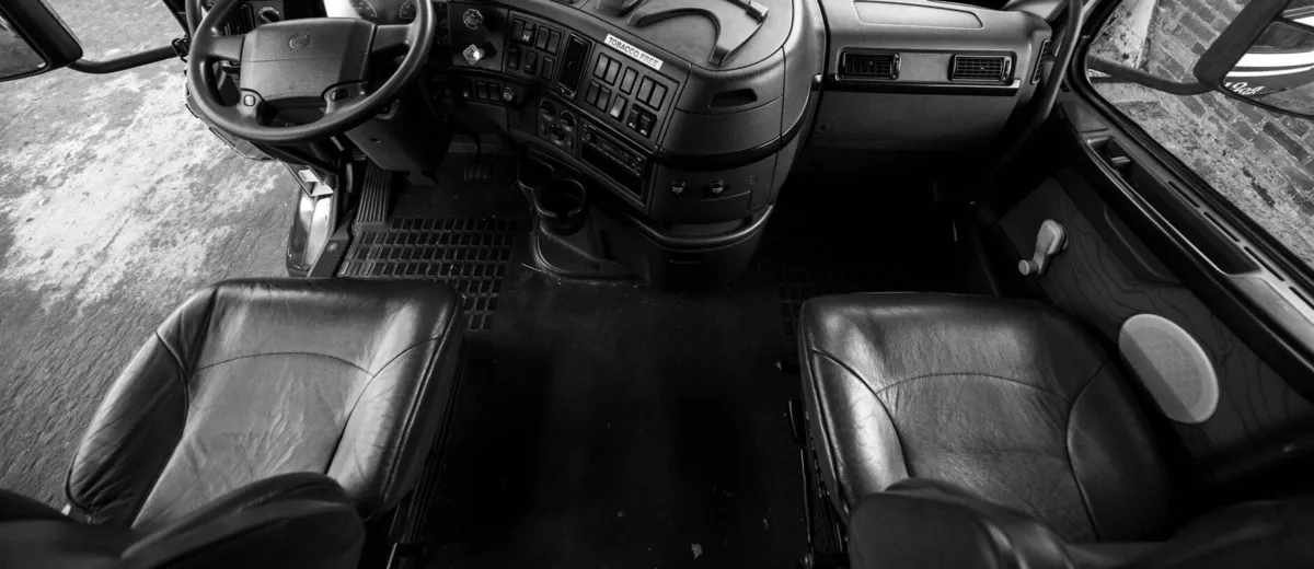 Due sedili di guida vuoti e un volante in una cabina di camion, ripresi dall’alto, in bianco e nero