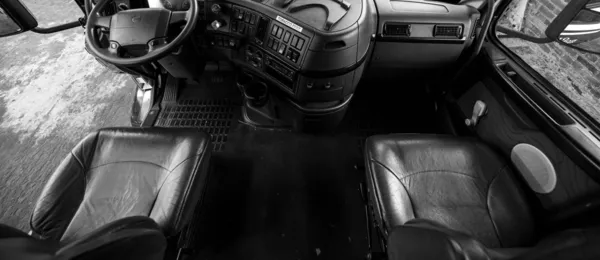 Due sedili di guida vuoti e un volante in una cabina di camion, ripresi dall’alto, in bianco e nero