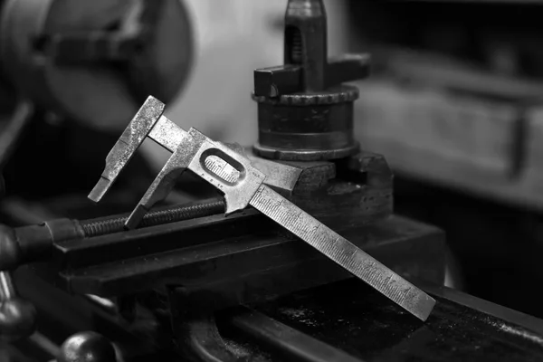 A vernier caliper resting on the slide of a workshop lathe, in black and white