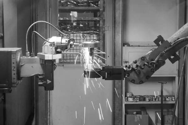 Un braccio robotico industriale al lavoro in una cella di saldatura, ripreso in bianco e nero