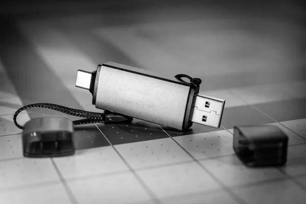 Chiavetta USB doppia, USB-A e USB-C, con i cappucci rimossi appoggiati accanto, su un tappetino a griglia, fotografia in bianco e nero
