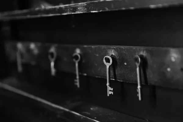 Cinque vecchie chiavi di metallo appese a ganci su una rastrelliera di legno scuro, fotografia in bianco e nero, sfondo sfocato