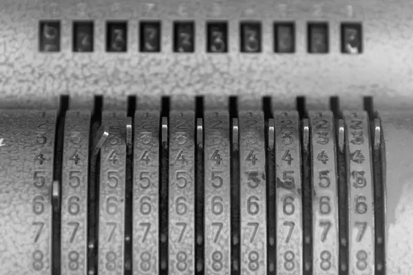 Primo piano in bianco e nero del meccanismo a cifre di una macchina calcolatrice meccanica d’epoca: colonne di numeri incisi nel metallo e leve di impostazione, nessuna scritta, nessuna persona