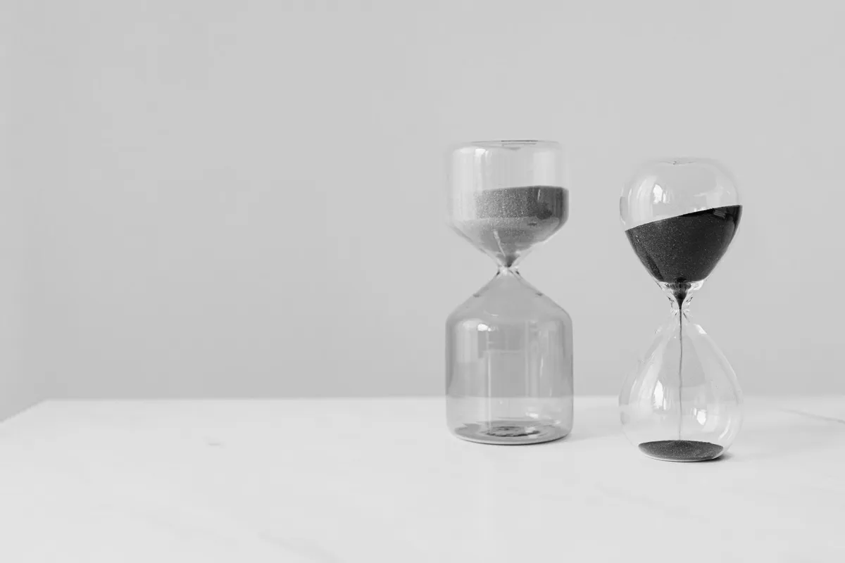 Two glass hourglasses on a light shelf, with sand at different levels, photographed in black and white