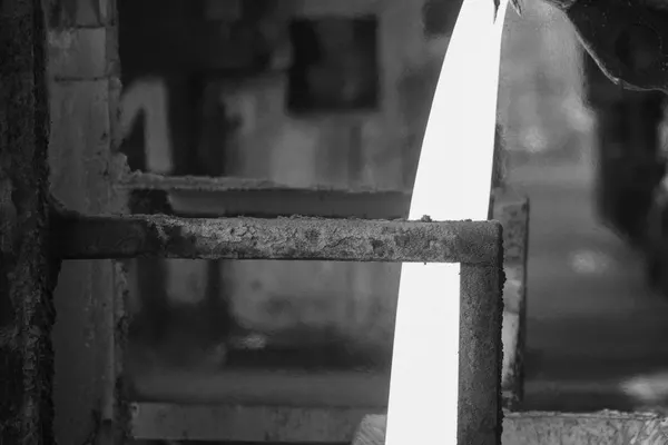 Colata di metallo fuso incandescente che scorre verticalmente tra strutture industriali arrugginite, fotografia in bianco e nero