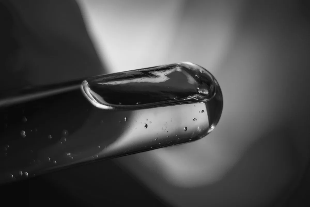 Punta di un contagocce di vetro in macrofotografia, con il liquido all’interno e alcune bolle minuscole, fotografia in bianco e nero