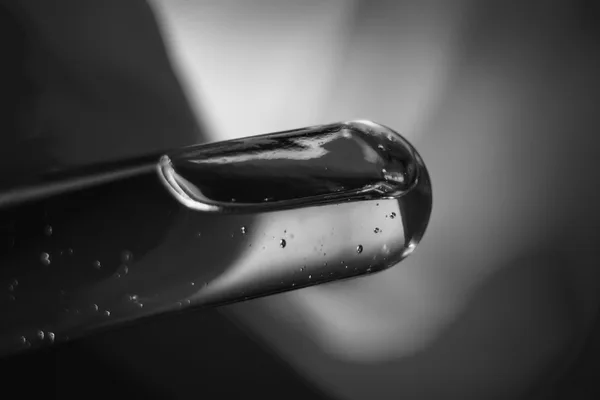 Punta di un contagocce di vetro in macrofotografia, con il liquido all’interno e alcune bolle minuscole, fotografia in bianco e nero