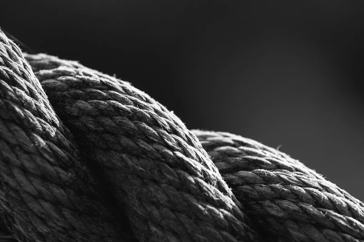 Close-up black-and-white photograph of a thick rope made of twisted strands, backlit texture