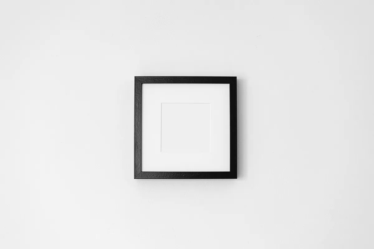 Empty black picture frame hanging on a white wall, black-and-white photograph