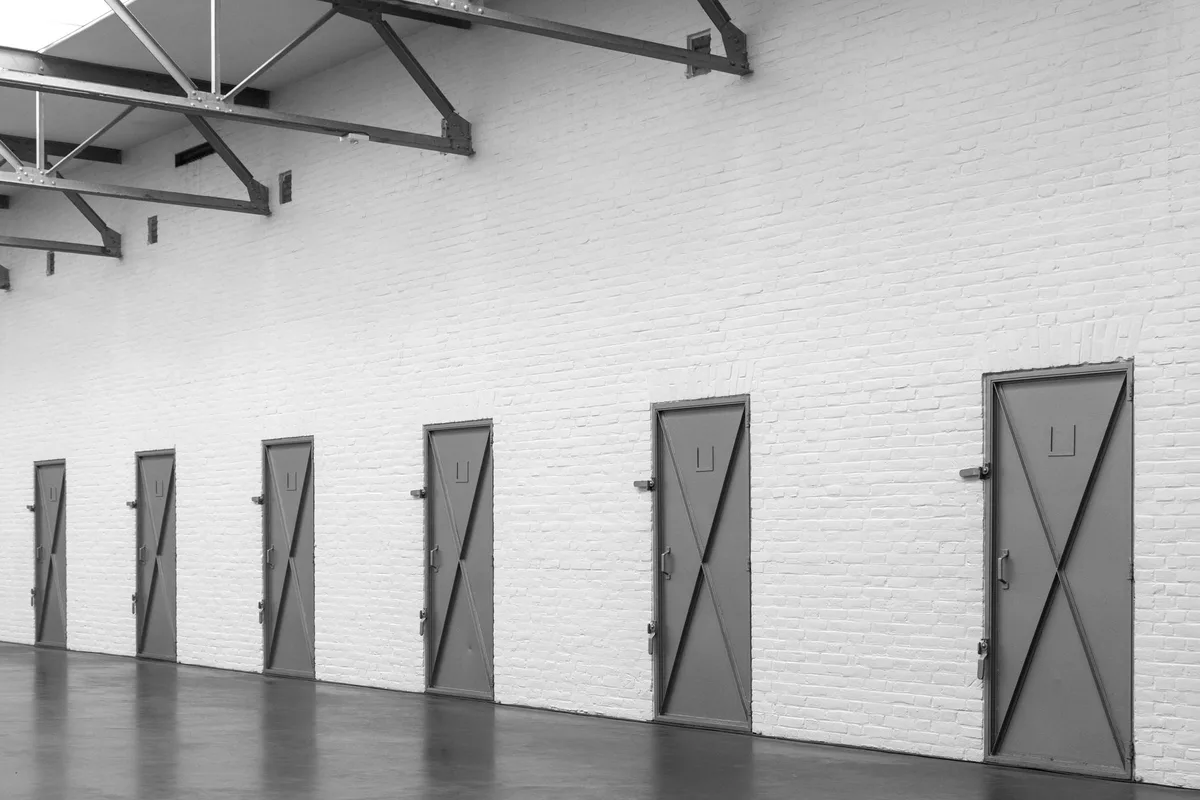 A row of grey armoured doors lined up along a white-walled corridor, photographed in black and white