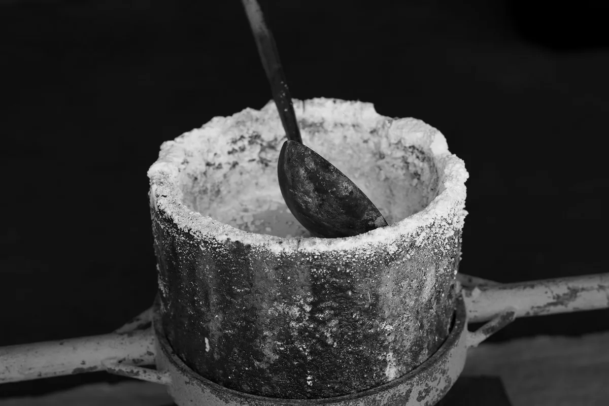 Crogiolo da fonderia incrostato, con un mestolo appoggiato all’interno, fotografia in bianco e nero
