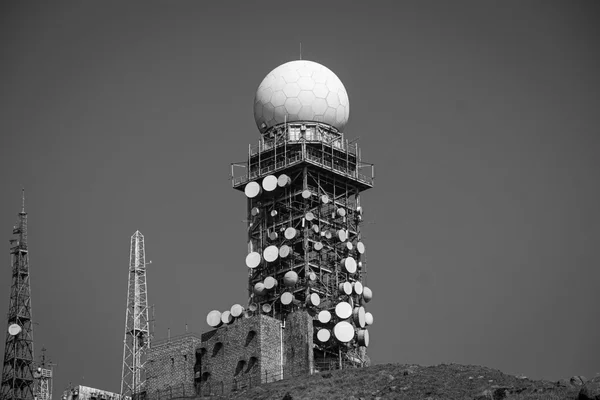 Torre radar con cupola sferica e decine di parabole di trasmissione puntate in direzioni diverse, contro un cielo intenso, fotografia in bianco e nero