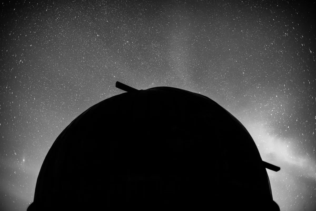 The dome of an astronomical observatory silhouetted against a night sky full of stars, in black and white