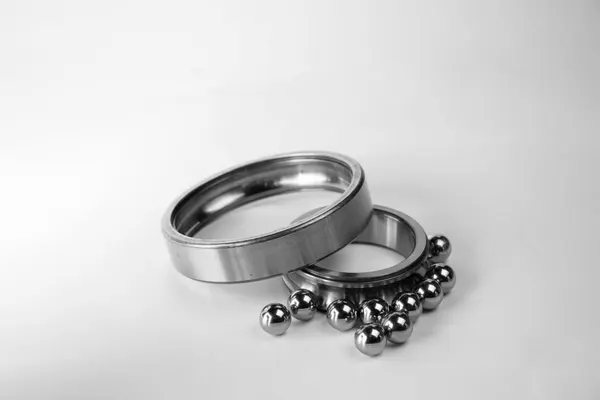 Due anelli di un cuscinetto a sfere smontato, uno intero appoggiato sull’altro da cui sono fuoriuscite alcune sfere metalliche, fotografia in bianco e nero