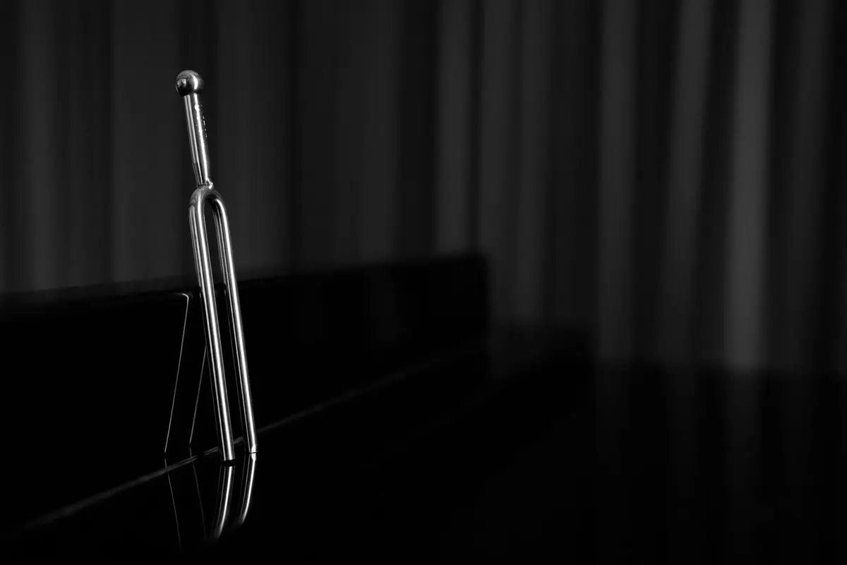 Un diapason d’acciaio poggiato su una superficie lucida scura, in penombra, fotografia in bianco e nero, nessuna persona