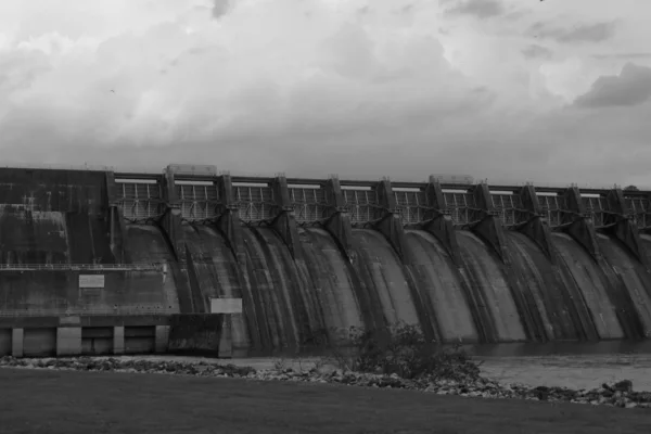 A concrete dam with a long row of spillway gates, under a heavy cloudy sky