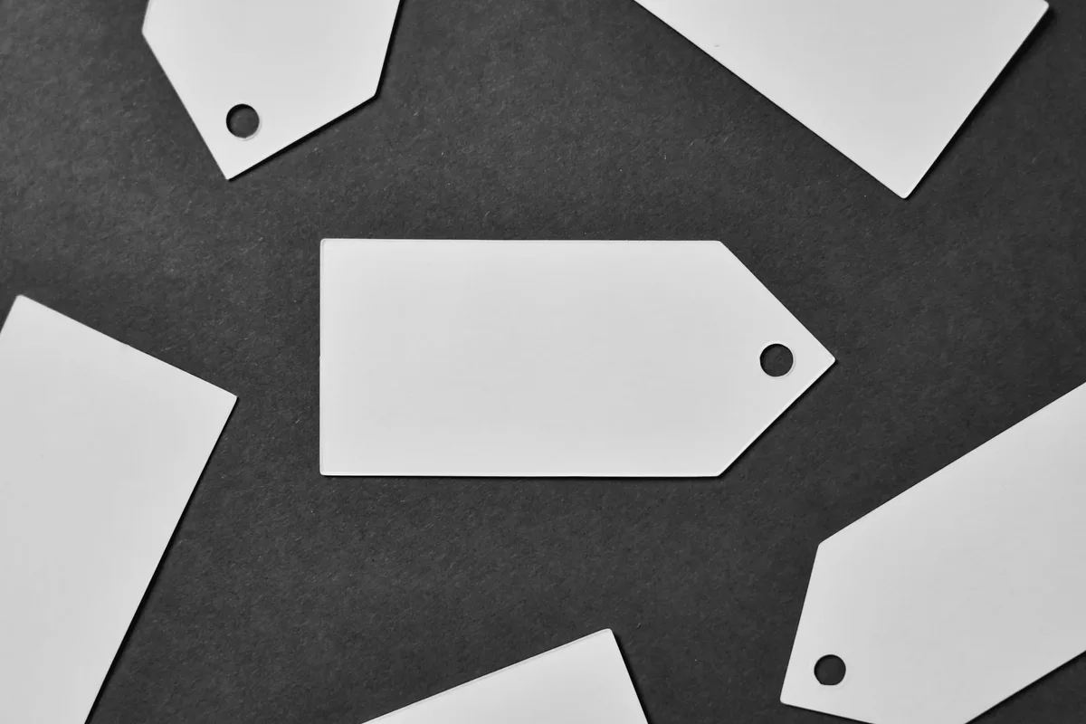 Blank white cardboard tags, empty and unmarked, scattered against a dark background, in black and white