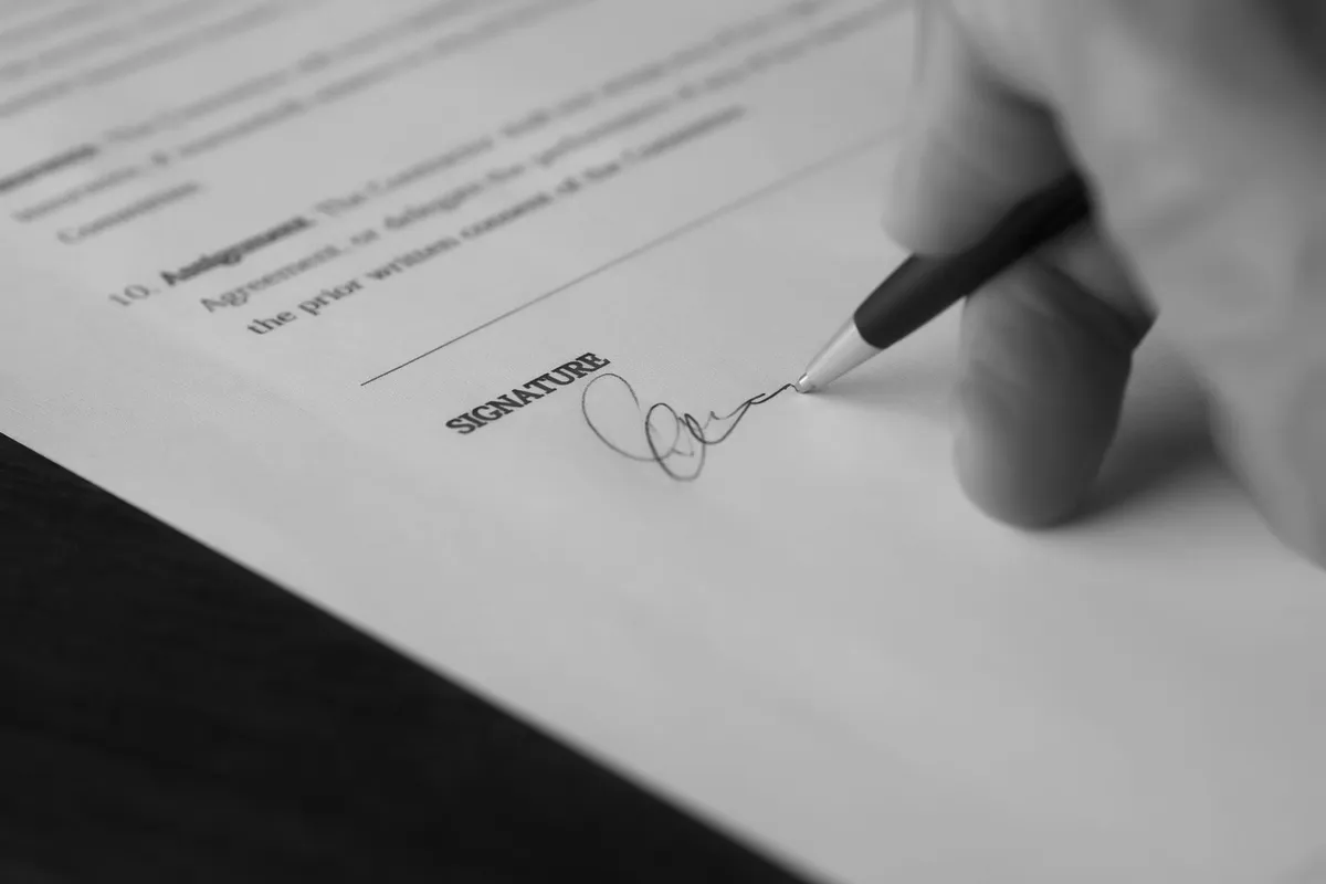 Mano che firma un documento con una penna, primo piano, in bianco e nero