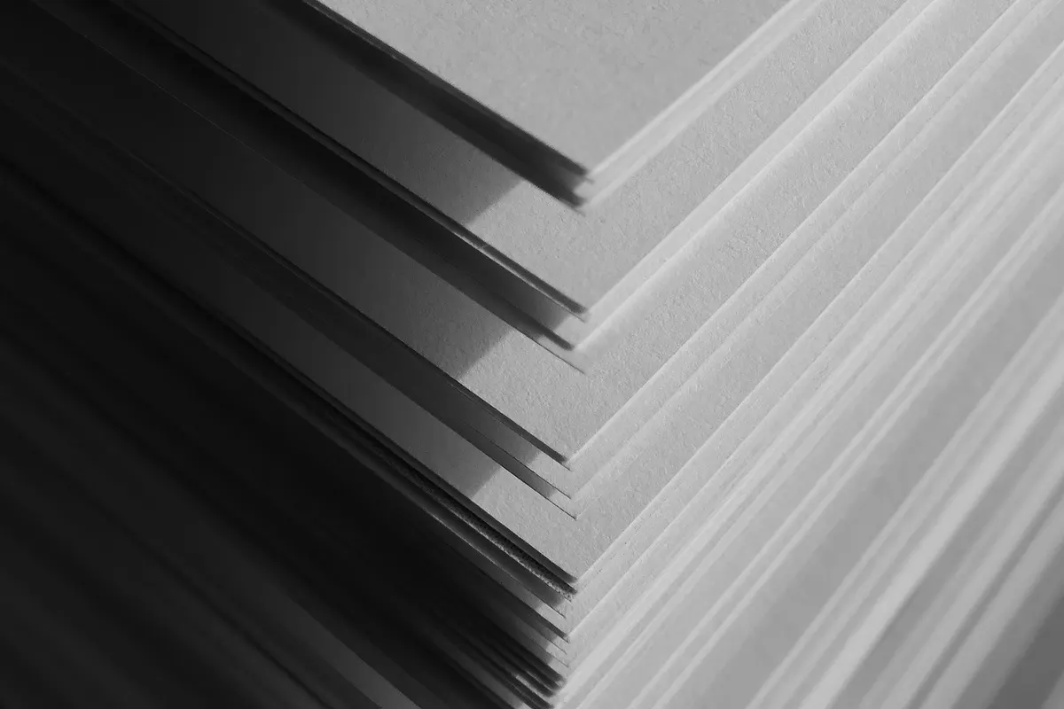 Corner of a stack of overlapping sheets of paper in strong backlight, close-up detail, black-and-white photograph