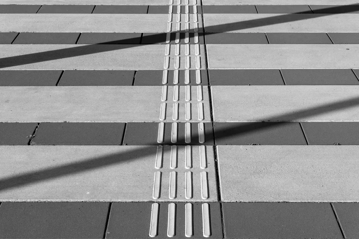 A row of raised tactile paving strips running in a straight line across light and dark paving slabs, black and white photograph, high contrast