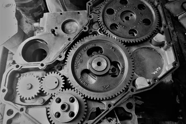 Timing gear train of an engine with the cover removed, casting numbers legible on the toothed wheels, in black and white