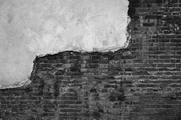 Uno strato di intonaco chiaro che si stacca da un muro di mattoni scuri sottostante, fotografia in bianco e nero ad alto contrasto