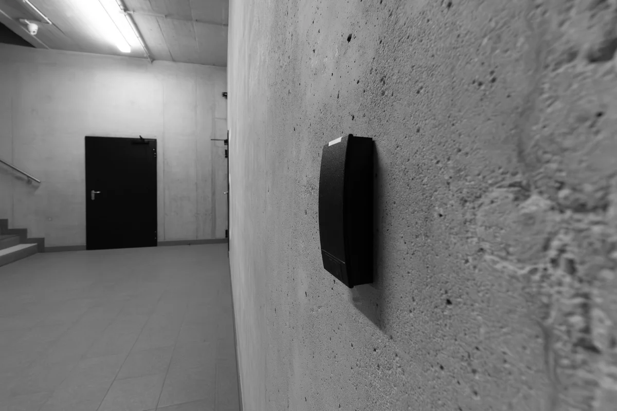 Lettore biometrico anonimo su una parete di cemento grezzo in un corridoio vuoto, in bianco e nero