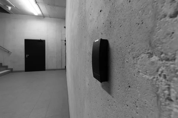 Lettore biometrico anonimo su una parete di cemento grezzo in un corridoio vuoto, in bianco e nero