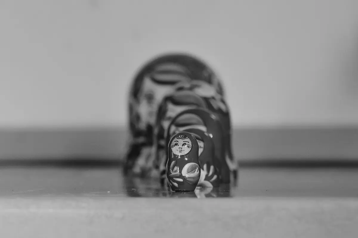 A row of painted wooden matryoshka dolls lined up, from the smallest in sharp focus at the front to the largest blurred in the background, black-and-white photograph
