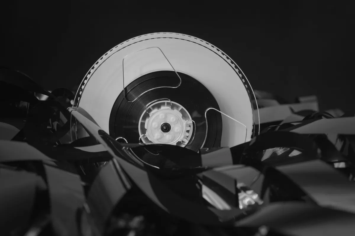 A tape reel unspooled over a heap of loose tape, photographed in black and white against a dark background