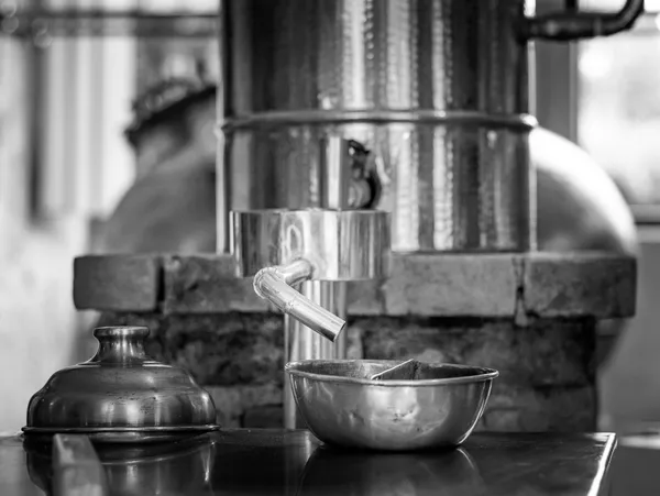 Alambicco di rame in una distilleria, con il beccuccio del condensatore rivolto verso una ciotola vuota, in bianco e nero