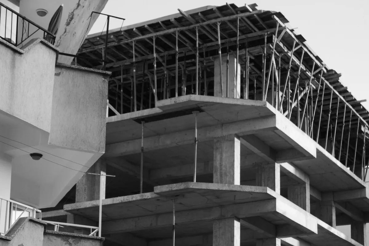 Struttura in cemento armato in costruzione, con puntelli e casseforme sull’ultimo solaio, in bianco e nero