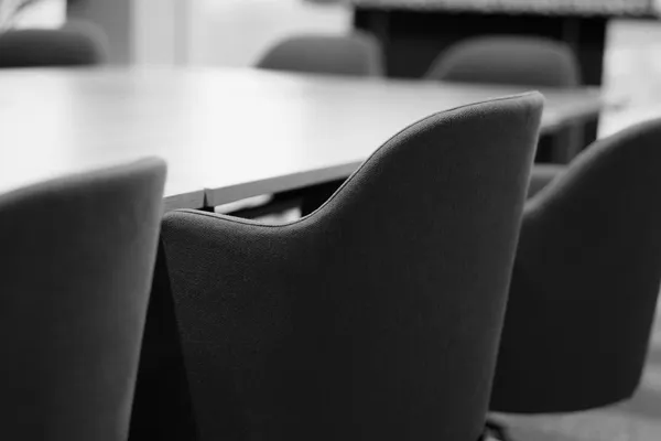 Schienali di sedie e un tavolo di una sala riunioni vuota, in bianco e nero