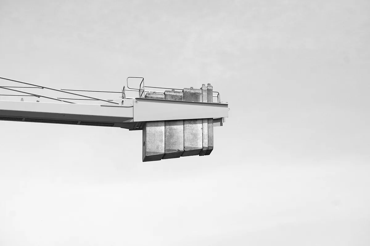 Concrete counterweight blocks hanging under the jib of a tower crane against the sky, black and white photograph