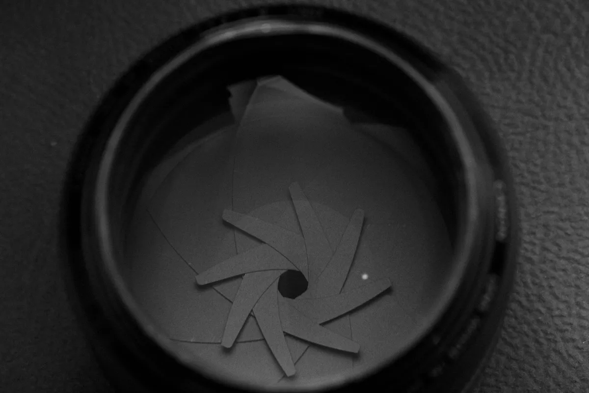 Diaframma di un obiettivo fotografico chiuso a spirale attorno a un foro centrale, ripreso macro, in bianco e nero