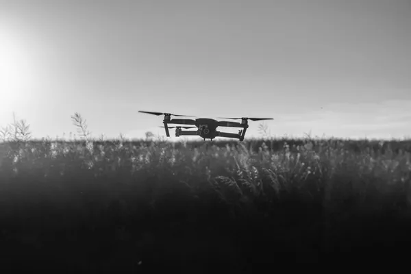 A drone backlit at sunset above a field, its silhouette showing no visible branding