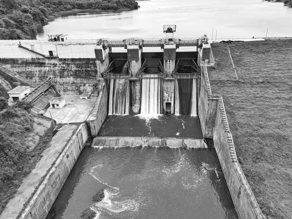 Sbarramento fluviale con paratoie metalliche aperte e acqua che scende negli scivoli di scarico, ripreso dall’alto, in bianco e nero