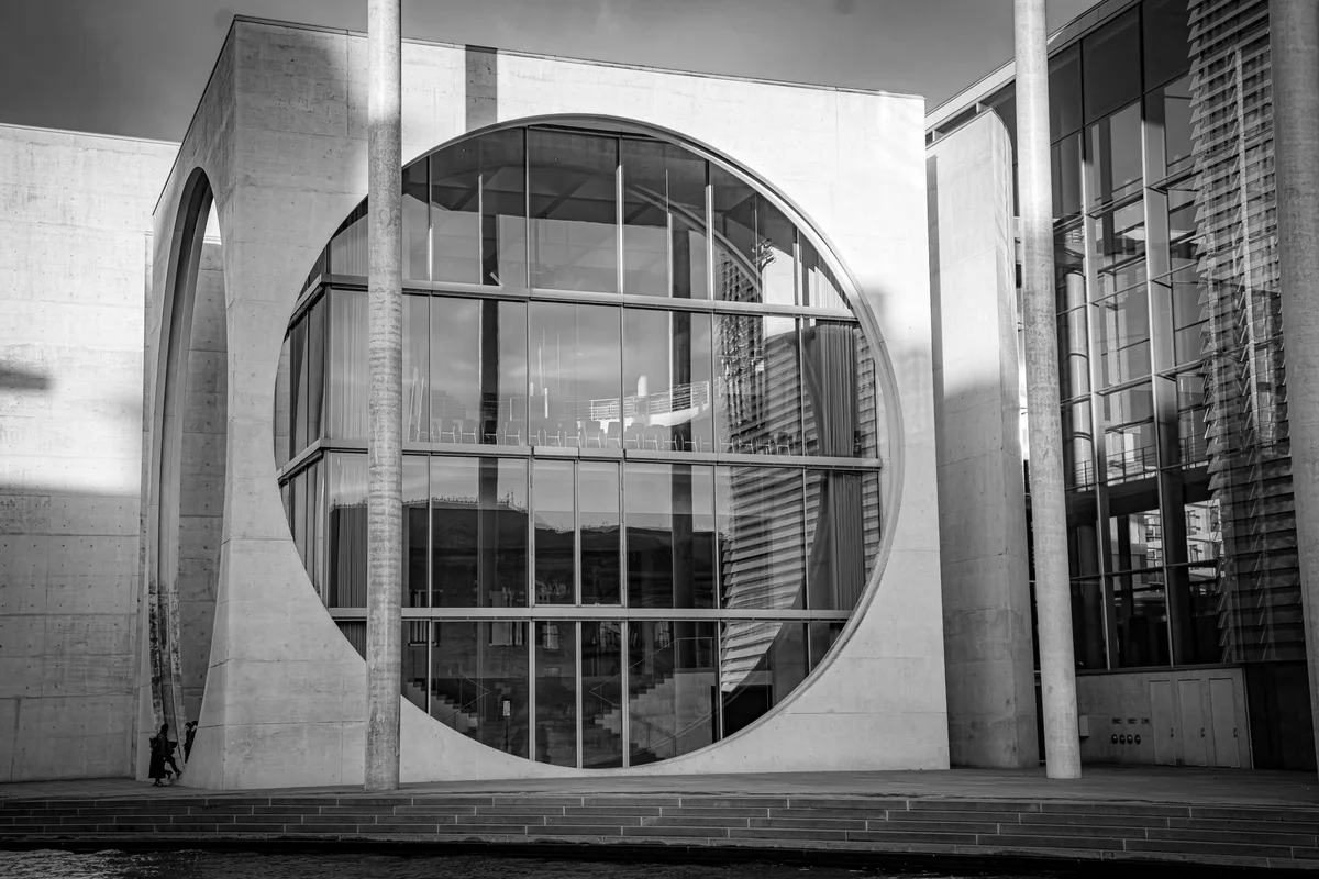 Façade of a modern institutional building in glass and concrete, with a large circular opening