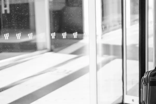 Ante in vetro di una porta girevole all’ingresso di un edificio, riflessi e ombre sul pavimento, fotografia in bianco e nero